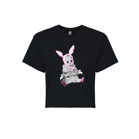 image of a women's black cropped tee on a white background. tee has center chest print of a baby doll sitting with pink bunny ears on its head. across the doll in white says starcrawler