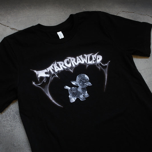 close up angled image of a black tee shirt laid flat on a concrete floor. front of tee has a center chest print of a chrome lamb. in chrome font at the top says starcrawler